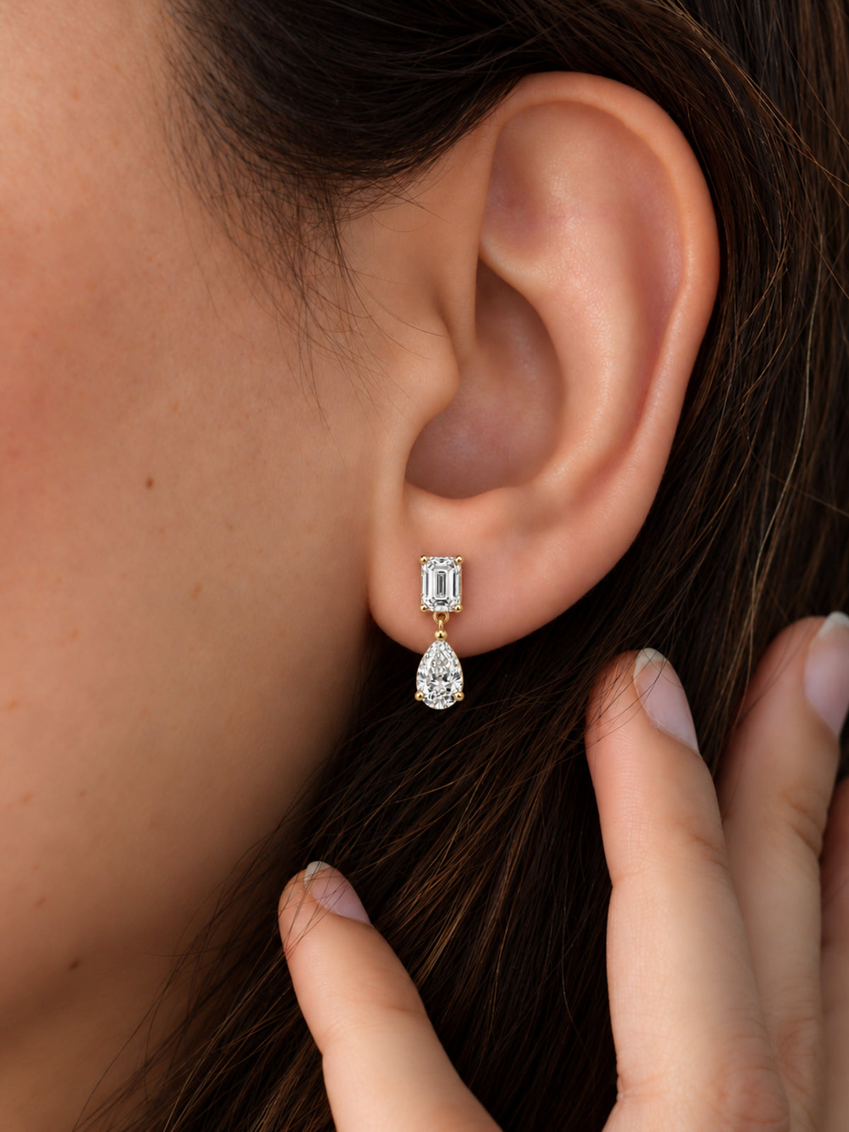 Emerald cut and pear lab diamond drop earring worn on ear